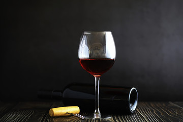 A glass of red dry wine on the table. Dark bottle and glass of wine.