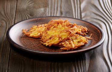 Fresh homemade tasty potato pancakes in clay dish on rustic wooden table