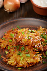 Fresh homemade tasty potato pancakes in clay dish with vegetables on wooden table