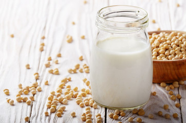 Non-dairy alternative Soy milk or yogurt in mason jar on white wooden table with soybeans in bowl aside