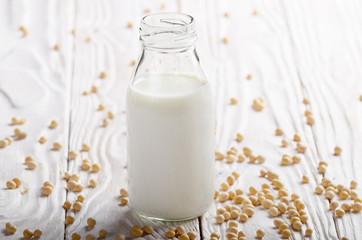Non-dairy alternative Soy milk or yogurt in glass bottle on white wooden table with soybeans aside