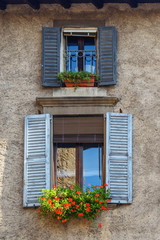 Fototapeta na wymiar Windows with shutters on facade of residential building with flowers on it. Bergamo. Italy