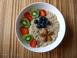 Breakfast bowl with strawberries, kiwi and blueberries, with cereals and almonds forming a flower.
