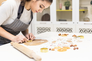 Young pretty woman prepares the dough and bakes gingerbread and cookies in the kitchen. She makes a star shape on the dough. Merry Christmas and Happy New Year.