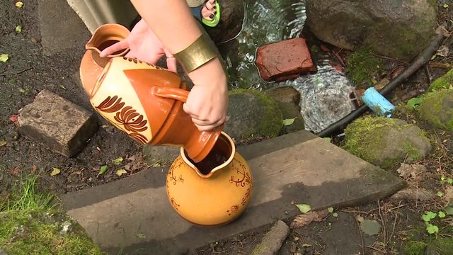 filling clay pitcher with clear forest spring water