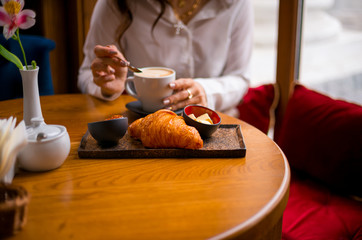 Cappuccino and croissant on a wooden table in the cafe in the morning.
