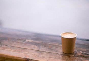A paper coffee cup with cappuccino in the street cafe on the wooden background. Place for text.