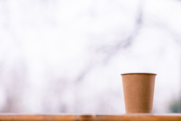 A paper coffee cup with cappuccino in the street cafe on the wooden background. Place for text.