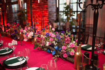 Fototapeta na wymiar Table wedding decor in red and black tones. Pink, blue and red flowers bouquet and candles in bottles.