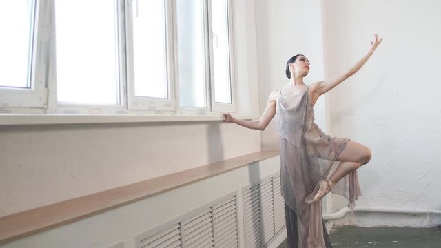 Beautiful ballet dancer in flying fabric dress, like the fabulous nymph lifting her leg up and stretching her arm forward during final reheasal before concert