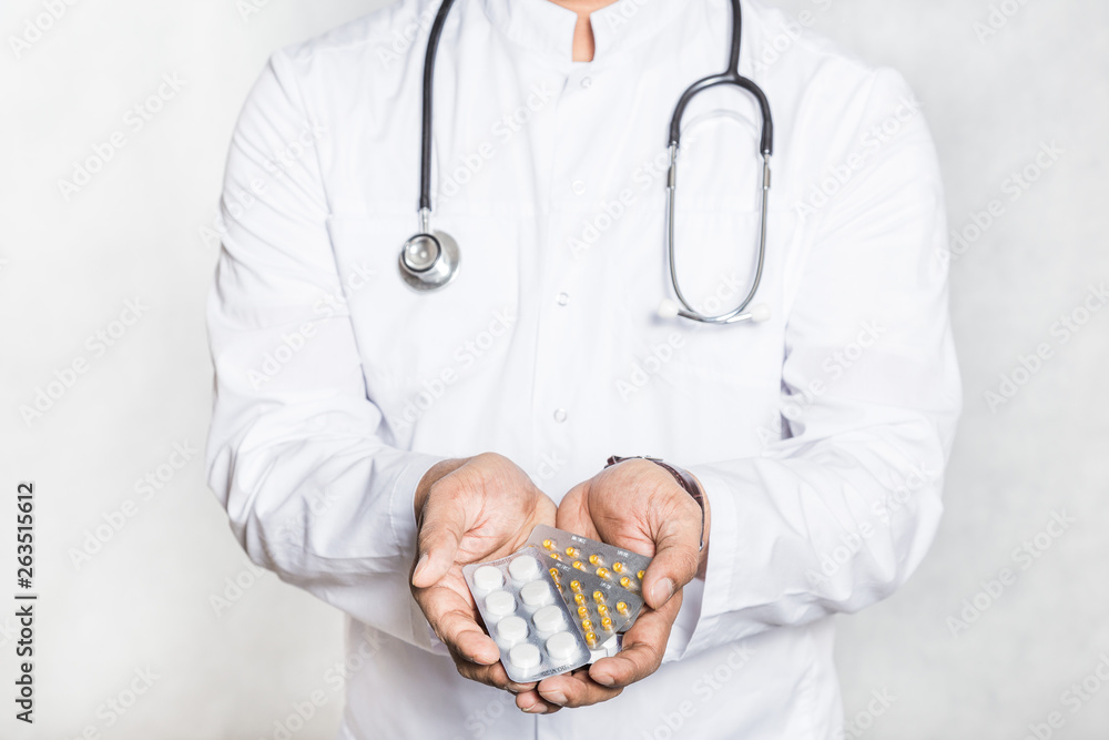 Canvas Prints Handsome young doctor in a white coat with a stethoscope holds on the outstretched hand a pills in blisters.