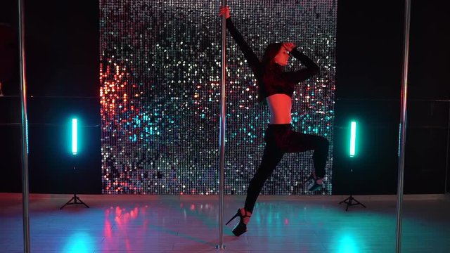 Alluring woman with long hair dancing with pylone on shining beautiful wall background. Sexy moving. Art, dance, sport concept