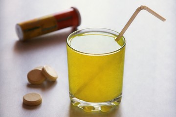 Water soluble tablet. Strengthens immunity with vitamins. Yellow drink in a glass beaker on a white background.