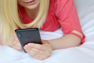 Blonde woman with smartphone, happy girl using mobile phone on the bed. Concept of online addiction, social media, sms messages, sex dating, internet