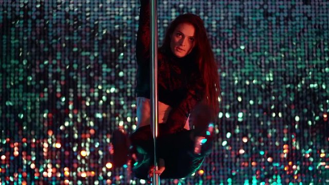 Alluring woman with long hair dancing with pylone on shining beautiful wall background. Sexy moving. Art, dance, sport concept