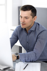 Fototapeta premium Businessman working with computer in modern office. Headshot of male entrepreneur or company director at workplace. Business concept