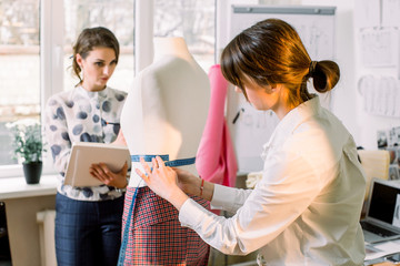 Back view of female dressmaker measuring mannequin with tape in atelier office. Talented fashion...
