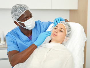 Doctor in mask is doing injection to woman patient in skin of face in estetic clinic