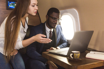 Obraz premium Young successful African-American businessman with glasses and an attractive female workmate blonde in a private jet. Service and flight first class