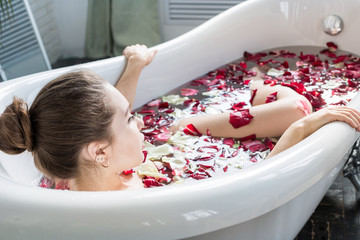 A young attractive girl takes a bathroom with flower petals and relaxes against the background of a...