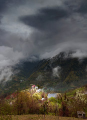 Fototapeta na wymiar Caucasus village and mountains on dark moody day with big clouds.