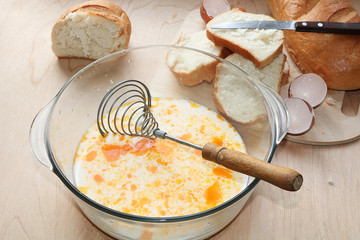A cup of milk with eggs and pieces of white bread, the process of cooking fried toasts. A working mess in the kitchen during the preparation of a delicious lunch