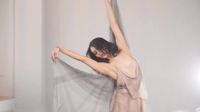 Adorable dark-haired ballet dancer in grey fishnet fabric costume with cape dancing in expressive manner over white background