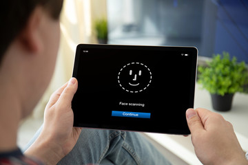 man hands holding computer tablet with face ID scanning