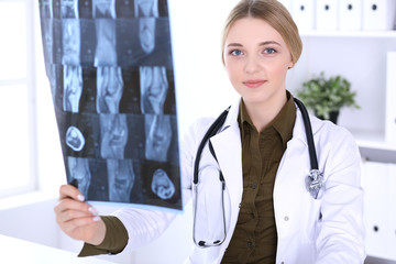 Doctor woman examining x-ray picture near window in hospital. Surgeon or orthopedist at work. Medicine and healthcare concept. Khaki colored blouse of a therapist looks good