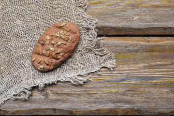 whole wheat bread with sunflower seeds and burlap on wooden background, top view 
