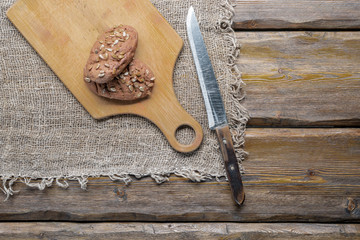 whole wheat bread with sunflower seeds and knife with cutting board and burlap on wooden background, top view 