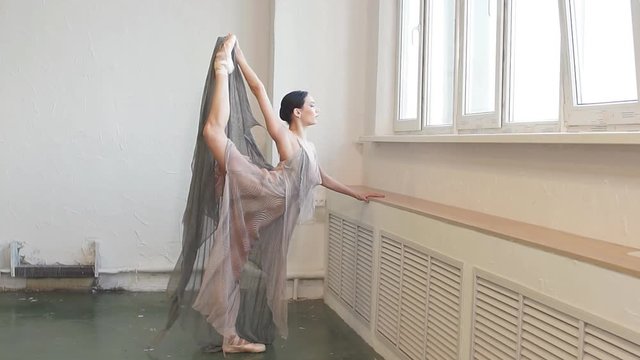 Beautful ballet dancer in flying fabric dress, like the fabulous nymph lifting her leg up and stratching her arm forward during final reheasal before concert