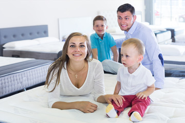 Smiling woman with husband and sons testing mattress in store