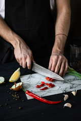 Slicing fresh red chili pepper with a knife on a cutting board. Chef cooking at a kitchen. Salsa, guacamole preparation. Mexican food.