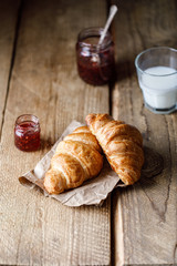 Freshly baked croissants with jam on wooden rustic background. Tasty croissants with copy space