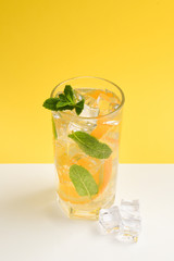 Cocktail with lemon and mint on a yellow background. Copy space.