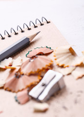 A notebook, a sharpener, shavings and pencils on a white background