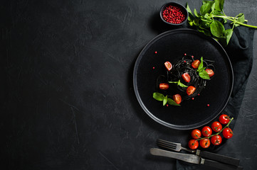 Black spaghetti with Basil and cherry tomatoes, vegetarian pasta. Black background, top view, space for text.