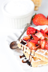 Belgium waffers with sugar powder, strawberries and chocolate on ceramic plate on white table.