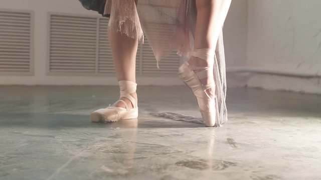 Close up of a ballet dancer s feet as she dancing in pointe shoes. Ballerina in stage long flowing dress shows classic ballet pas.