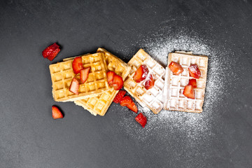 Belgium waffers with strawberries and sugar powder on black board background.