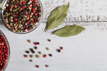 Assorted pepper spices. Pepper mix. Black, red and white peppercorns and dried bay laurel leaves on white wooden background. Seasonings for food