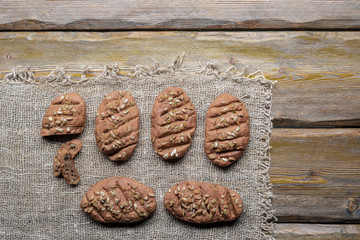 whole wheat bread with sunflower seeds and knife with cutting board and burlap on wooden background, top view 