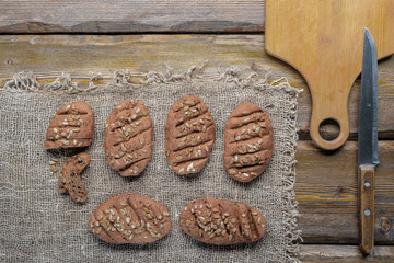 whole wheat bread with sunflower seeds and knife with cutting board and burlap on wooden background, top view