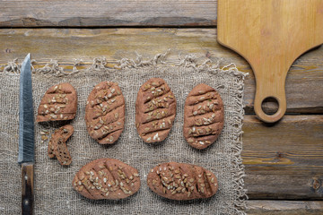 whole wheat bread with sunflower seeds and knife with cutting board and burlap on wooden background, top view 