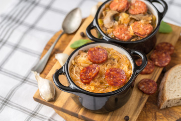 Slovak Christmas national cabbage soup in small black pot with sausage on the tablecloth background.