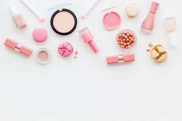 Make-up artist desk with powder, nail polish, decorative cosmetics and macaroon cookies white background top view mokeup