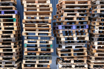 Stacks of colorful rough wooden pallets at warehouse in industrial yard. Pallets background. Cargo and shipping concept.