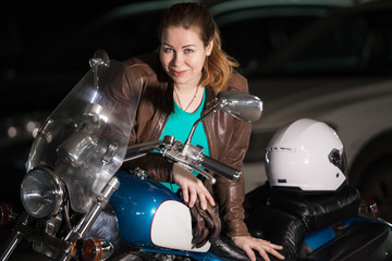 Plakat Biker girl portrait, young heavily-built woman standing near her motorcycle and white helmet in dark parking