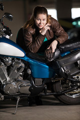 Fototapeta na wymiar Biker woman with a heavy build standing near her motorcycle, leaning the seat, looking at camera